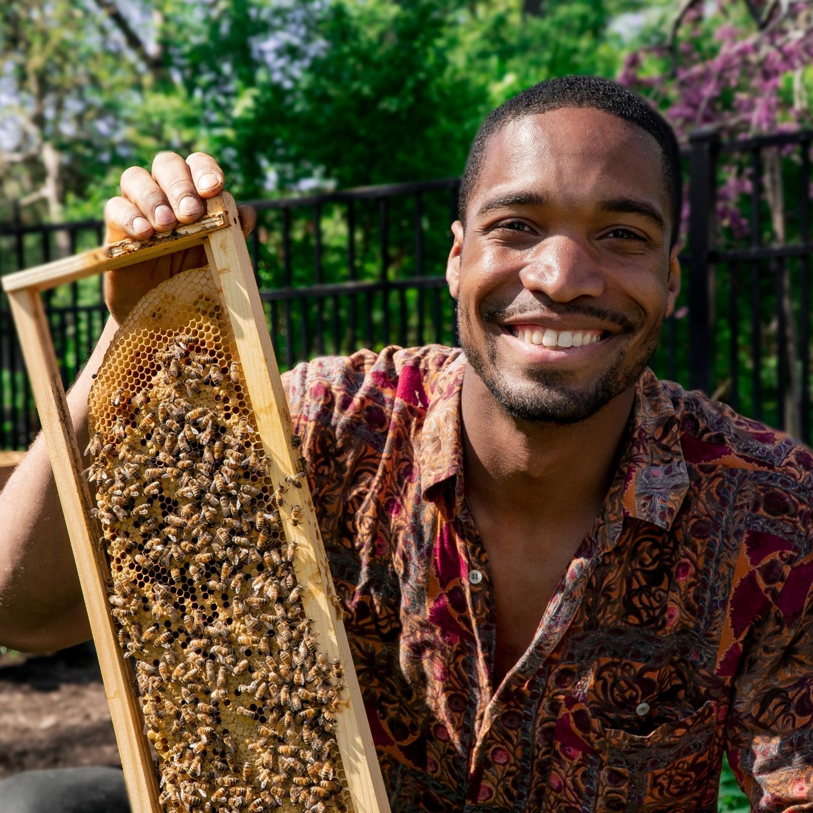 A picture of a black man, Brandon Reynolds, holding a rectangular bee hive.